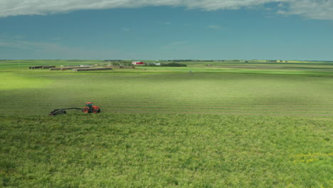 slow driving tractor busy swathing green hay into windrow,  panning around drone shot