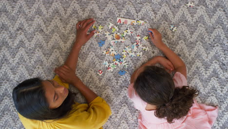 overhead shot of mother and daughter at home lying on floor in lounge doing jigsaw puzzle together