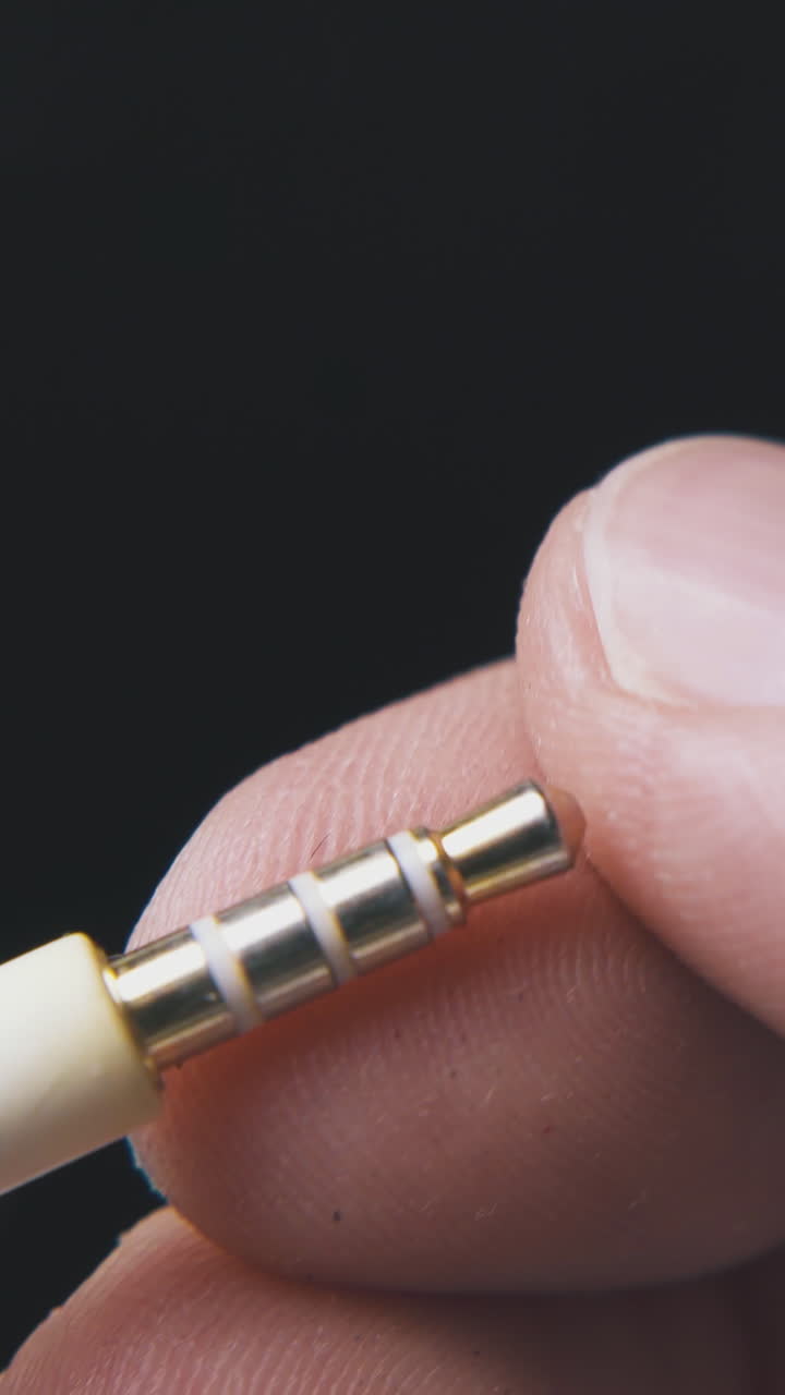 young person touches metal jack plug with beige cable on black background extreme close view
