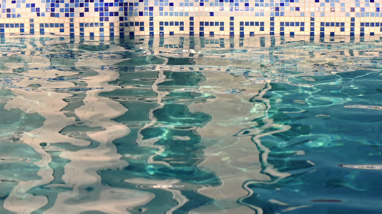 Bright sunlight dances on the shimmering water of a serene pool. The blue tiles create a beautiful contrast, inviting relaxation on a warm afternoon