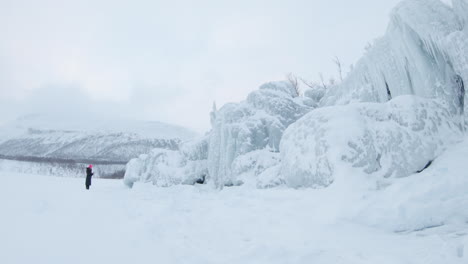 Girl-standing-in-front-of-a-big-iceberg-on-a-frozen-lake-in-Björkliden,-Sweden