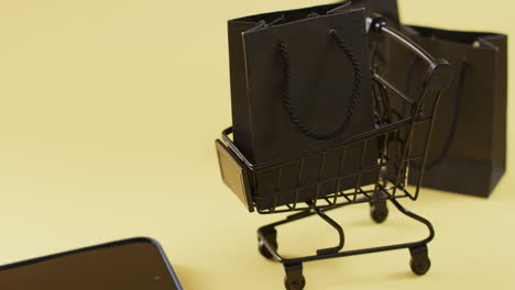 video de teléfono inteligente con pantalla en blanco, bolsas de compras y carrito, copia de espacio en fondo amarillo