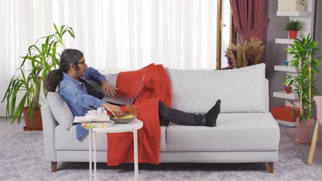 hombre en casa mirando la computadora portátil y comiendo papas fritas.