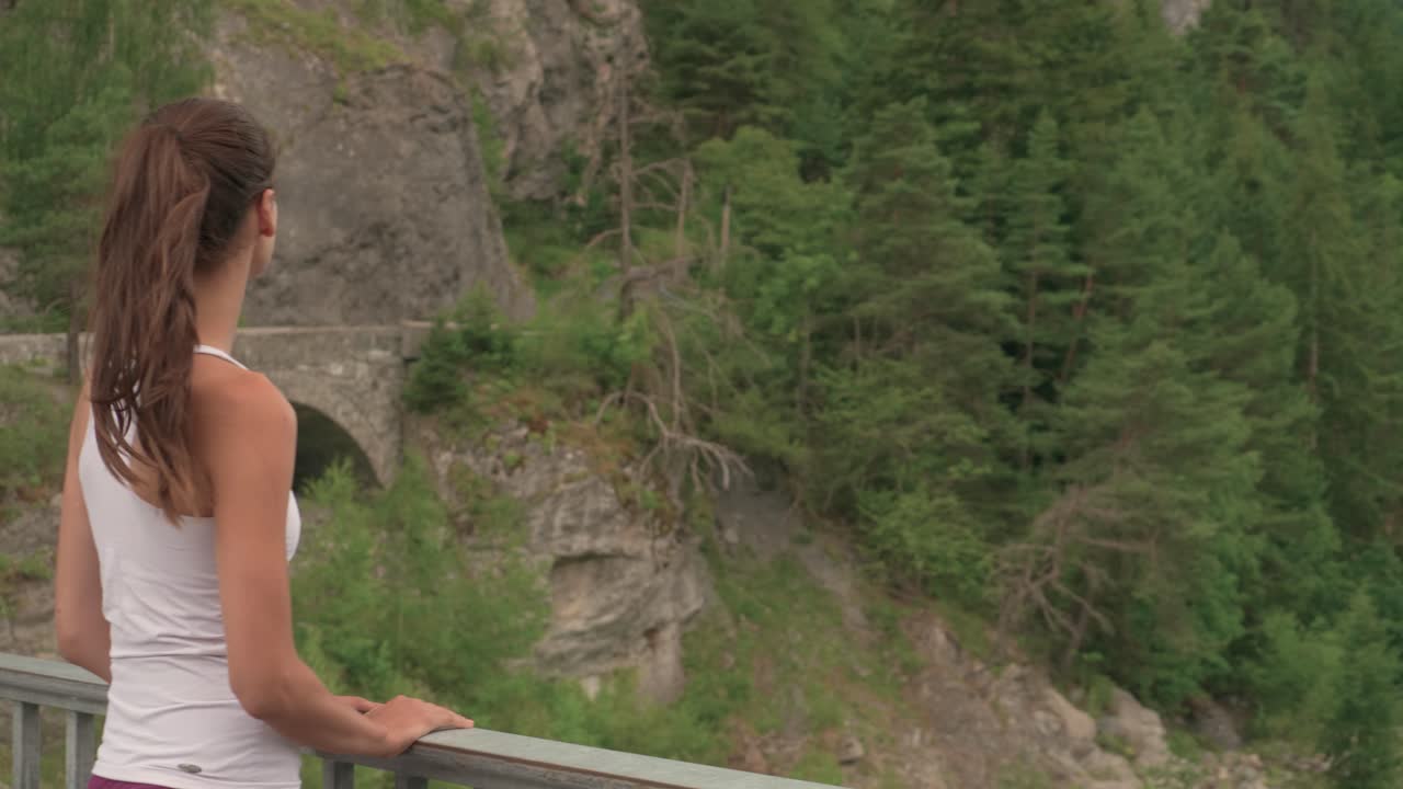 una mujer bonita se encuentra al borde de un acantilado con barandilla mirando hacia el desierto rocoso con una torre de construcción en la distancia
