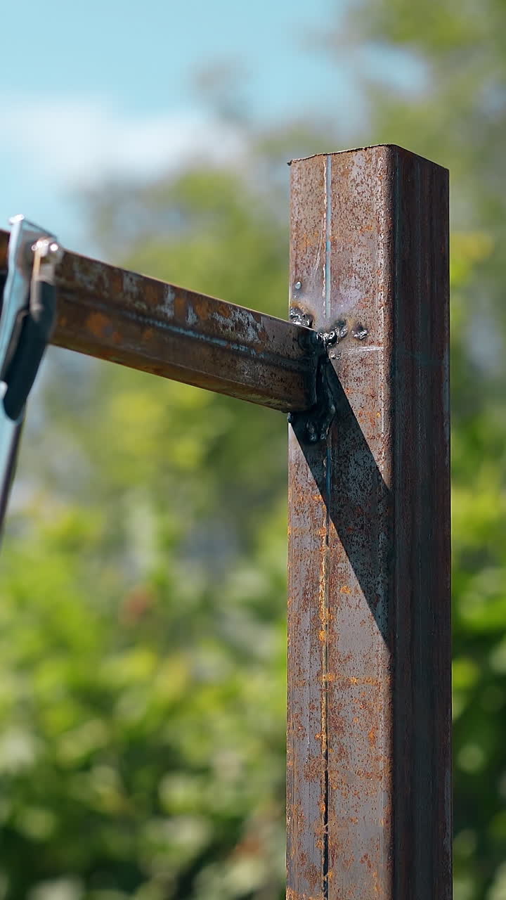 Primo piano di saldatore esperto in abbigliamento da lavoro che collega le parti superiori di una carcassa di recinzione arrugginita contro alberi verdi di giorno