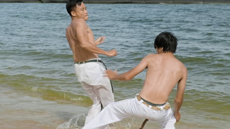 two men dancing capoeira on the beach