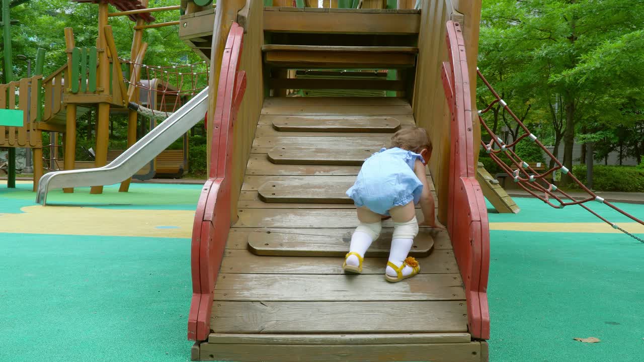 Little girl toddle all along at a playground in the park struggling to climb the ladder - Asian, multi-ethnic Korea-Ukrainian child