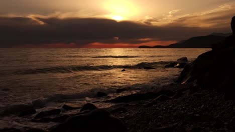 dramatic sunset with dark cloudy sky and orange colors reflecting on sea surface seen from shoreline of mediterranean