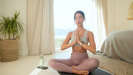 young woman meditating on yoga mat at home, feeling relaxed and peaceful