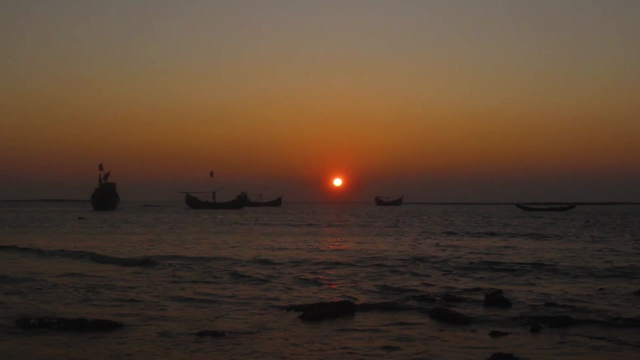 Timelapse of a beautiful sunset at the coastline of Saint Martin Island, Bangladesh. Traditional boats anchored in the sea, waves breaking on the shore rapidly