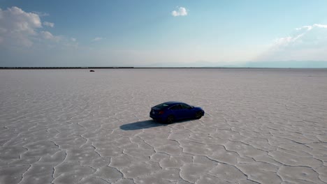 Aerial-drone-shot-following-a-black-sedan-car-over-Bonneville-Salt-Flats-in-Tooele-County-in-northwestern-Utah,-USA-at-daytime