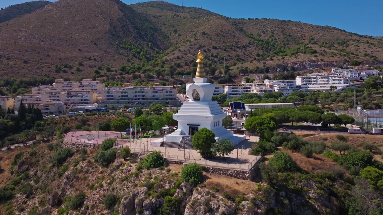Riprese con drone di Benalmádena, Andalusia, Spagna, che si avvicinano a una stupa bianca su pendii rocciosi con montagne aride, luce intensa e dintorni urbani tranquilli.