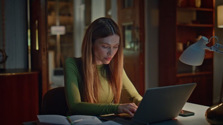 Kvindelig forfatter skriver på bærbar computer sent om aftenen, nærbillede. Kvinde kigger på computerskærm.