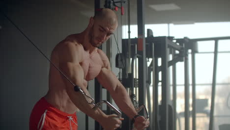 brutal handsome caucasian bodybuilder working out in the gym training chest pumping up pectoral muscles with dumbbells and on crossovers gaining weight and poses fitness and bodybuilding concept