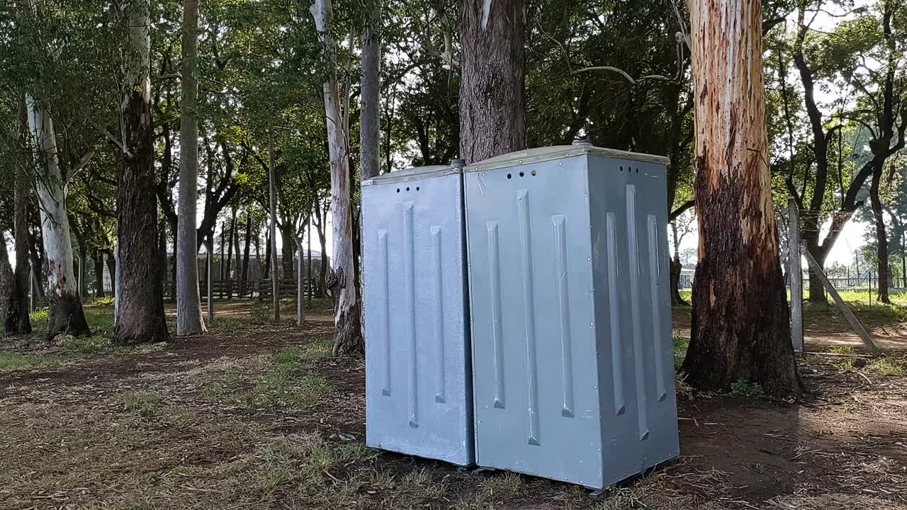 Close up shot of grey outdoors portable bathroom surrounded by forest of eucalyptus trees, It's sunny outside