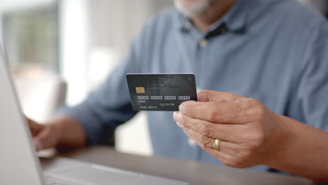 happy senior biracial man using credit card and laptop for online payment, slow motion