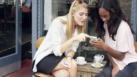 female friends sharing together using smartphone in urban cafe