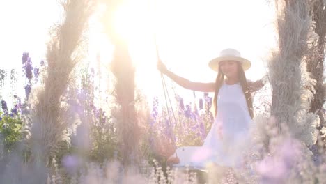 of a young woman in a white beautiful rustic dress is riding a rope swing a young woman in a white beautiful rustic dress is riding a rope swing suspended from an old oaktree wide view low angle view from ground throw grass freedom lifestyle concept slow motion shot