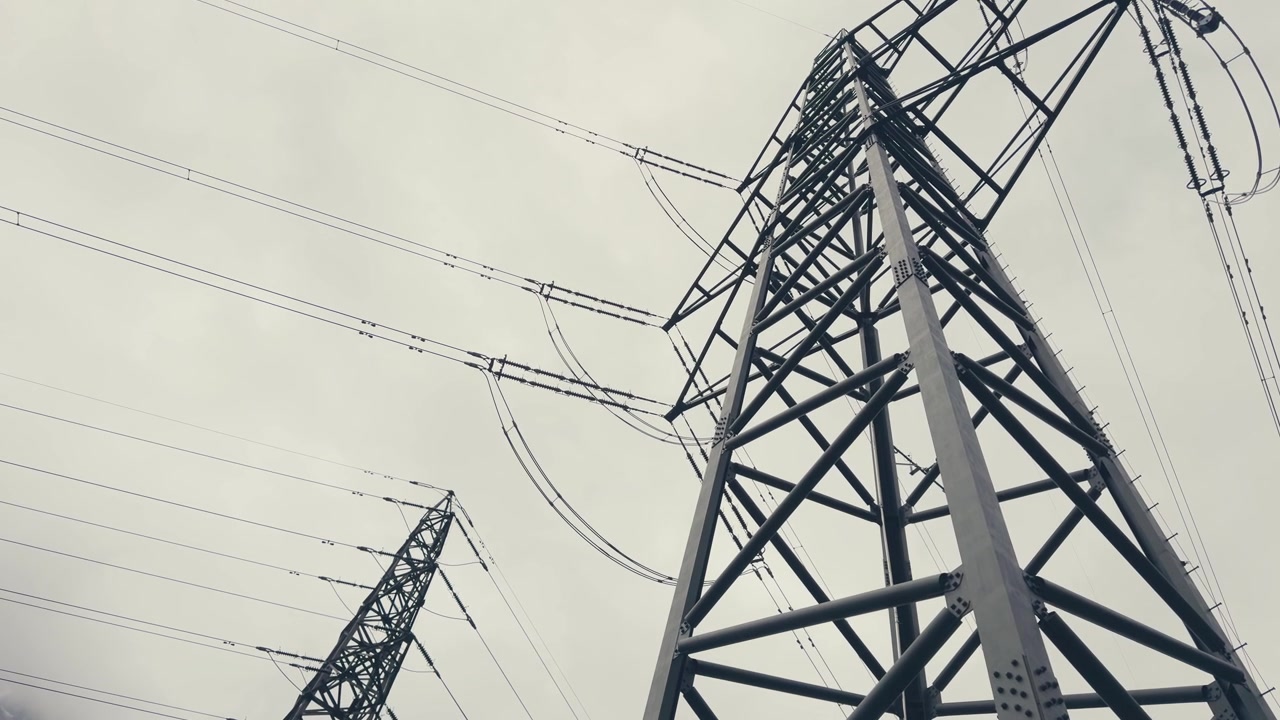 POV view looking upward at massive electricity pylons and transmission lines stretching into the sky. A dramatic perspective showcasing energy infrastructure, engineering and modern power networks.