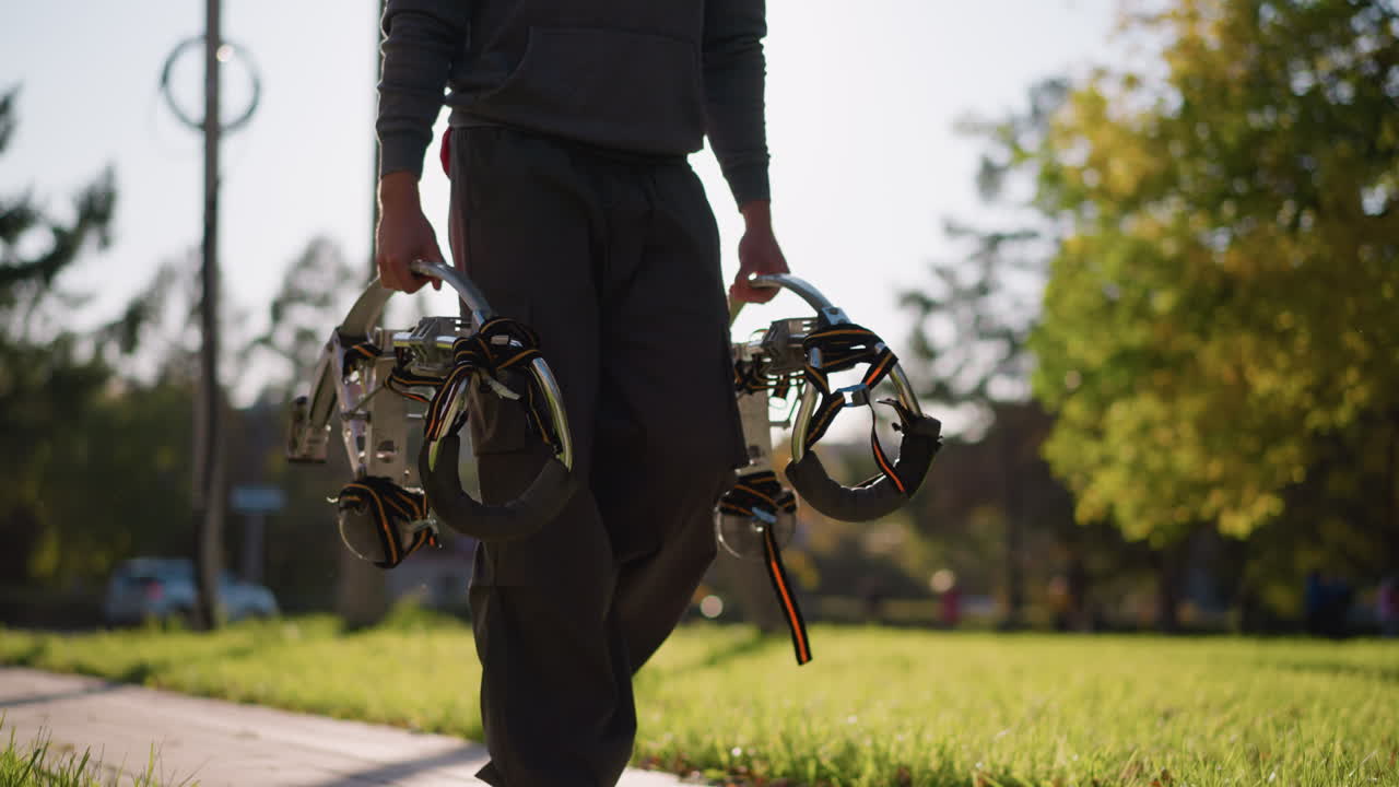 어두운 회색 또는 네이비 스웨트 셔츠와 어두운 바지를 입은 사람은 검은색 포장 된 발바닥과 오렌지색과 검은색 줄을 가진 금속 스을 들고 있습니다. 손은 스 프레임을 단단히 잡고, 목적을 가지고 고, 얼굴이 없습니다.