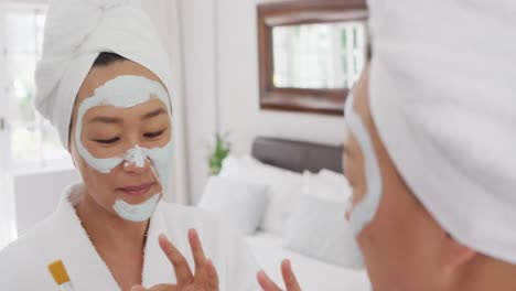 video of happy asian woman in robe with moisturizing mask looking at mirror