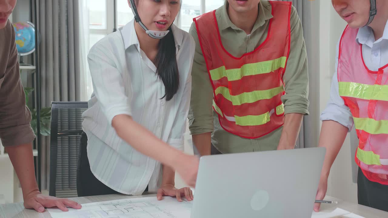 Three Asian Engineers With Helmets Using Laptop For Working To A Man At The Office