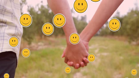 varios emoji de cara sonriente flotando contra la sección media de la pareja tomados de la mano