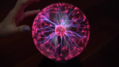 a female hand touches a plasma ball giving out small lightning bolts. experiments with electricity in the dark.