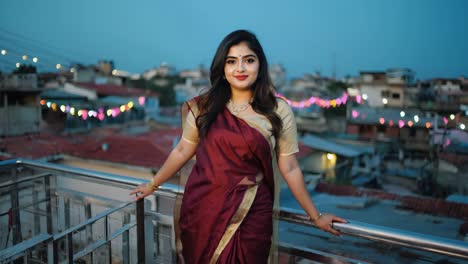 elegant indian woman wearing a traditional saree is posing on a rooftop at dusk, with colorful string lights illuminating the urban background