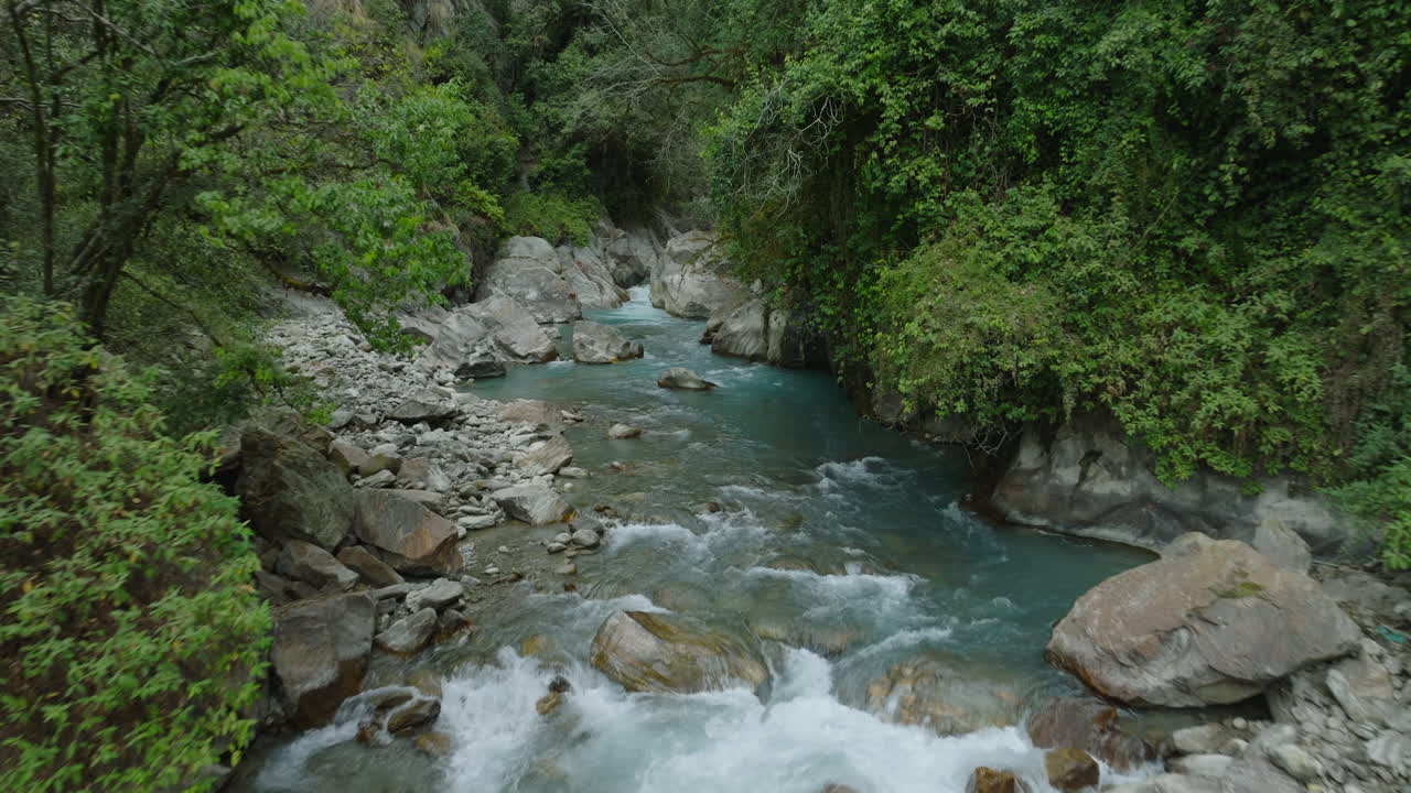 Ripresa con drone cattura un fiume che scorre silenziosamente nel paesaggio del Parco Nazionale di Langtang, Nepal. Circondato dalla vegetazione e che suggerisce il mistero della vita acquatica, la scena sembra quasi mitica.
