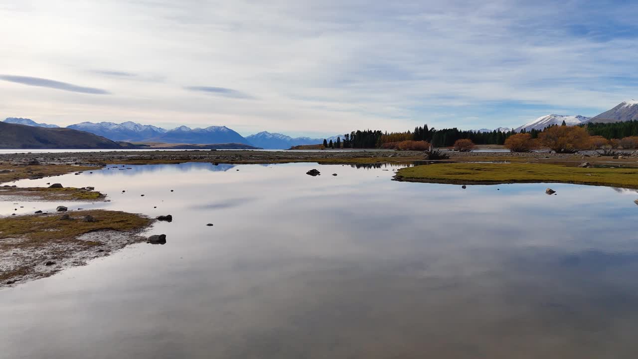 Aerial footage captures Lake Tekapo's serene landscape with reflective waters and autumn foliage under soft daylight