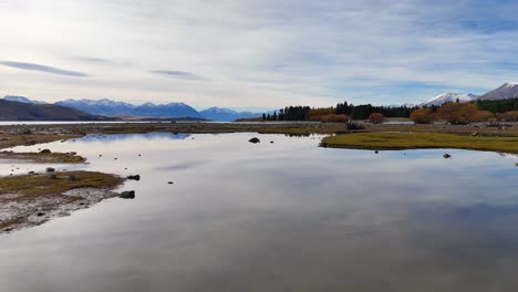 aerial footage captures lake tekapo's serene landscape with reflective waters and autumn foliage under soft daylight