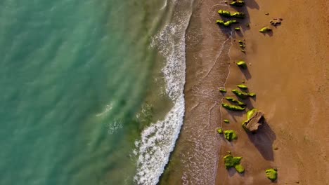 Luftlandschaft-Mit-Meereswellen,-Grünem-Wasser,-Warmem-Farblicht-Des-Sonnenuntergangs-Und-Der-Goldenen,-Friedlichen-Malerischen-Landschaft-Eines-Sandstrandes-In-Einer-Küstenklippenerosions-Felsformationslandschaft-Auf-Der-Insel-Hormuz,-Iran