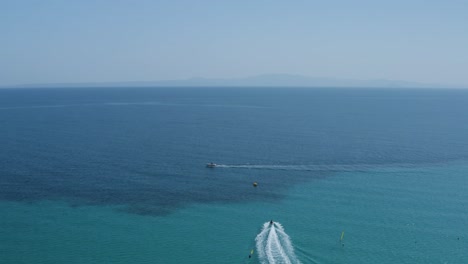 aerial drone shot backwards of boat and jet ski in clear blue sea