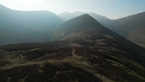 Hiker-alone-on-mountainside-with-reveal-of-misty-mountain-range-beyond-in-English-Lake-District-UK