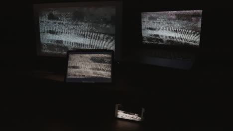 Four-digital-computer-device-screens-displaying-a-choppy-static-noise-pattern-in-a-dark-room