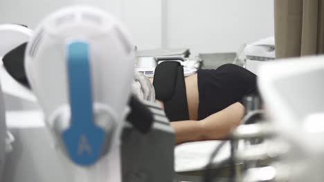 una joven clienta caucásica está utilizando el innovador procedimiento emsculpt no quirúrgico para tonificar el área de su abdomen quemando grasa y desarrollando músculos en una clínica de cosmetología