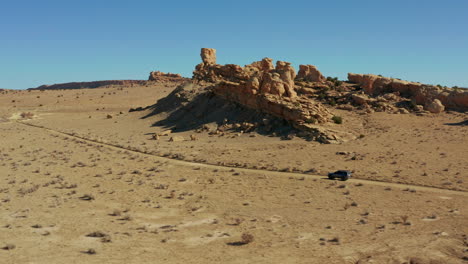 Szenische-Antenne,-Die-Dem-Auto-Auf-Der-Wüstenpiste-Mit-Hoodoo-Felsformationen-Folgt