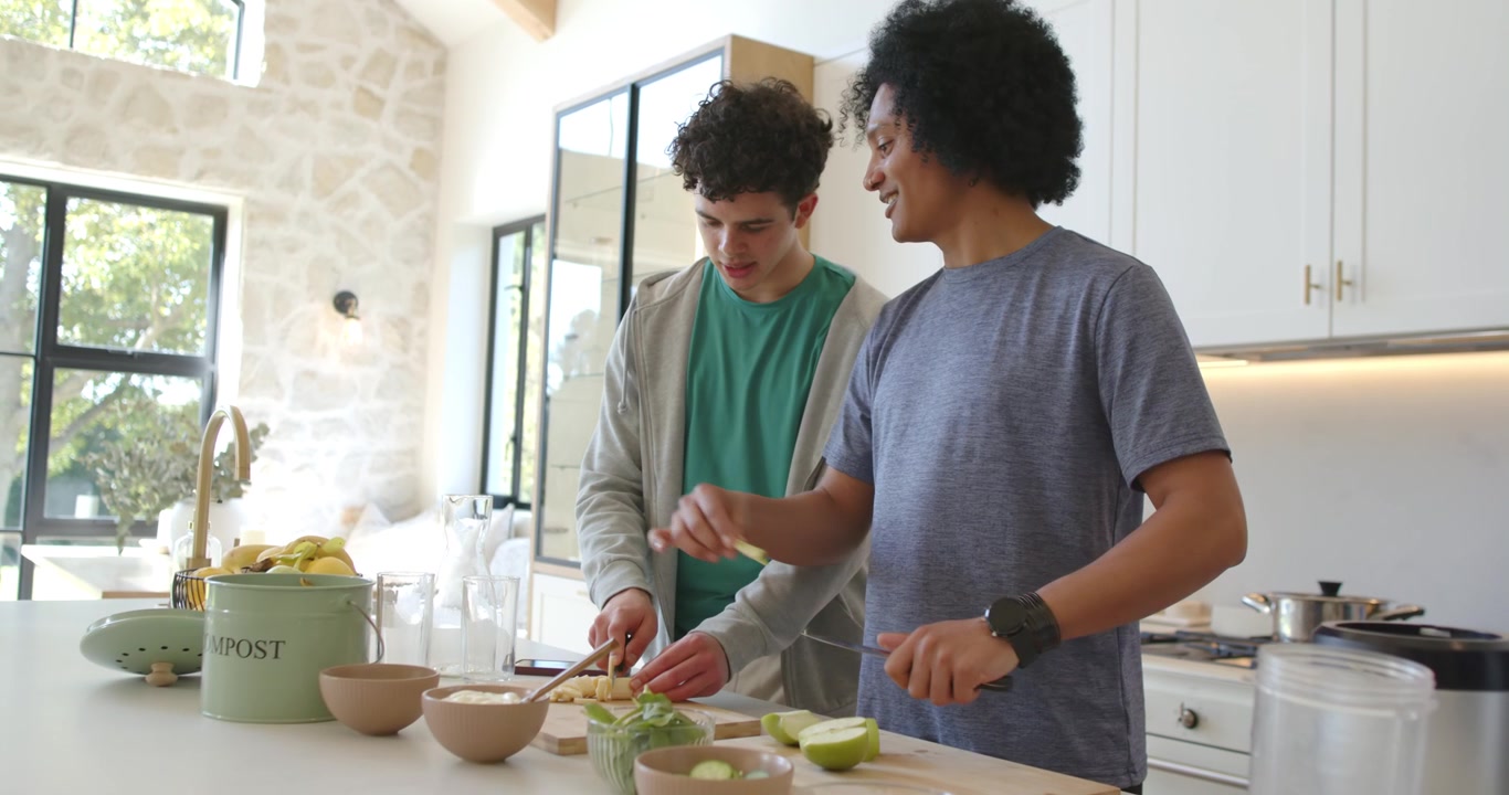 Uomini afroamericani intenti a tagliare la frutta sull'isola della cucina, mettendola in ciotole per uno spuntino.