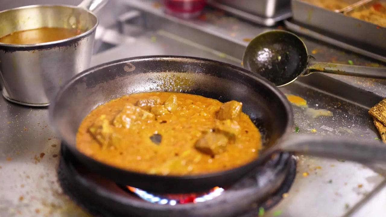 Primo piano di curry cremoso arancione che sobbolle su un fornello a gas in una cucina professionale di ristorante.