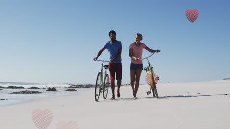 animation of hearts over happy african american couple walking with bikes on beach