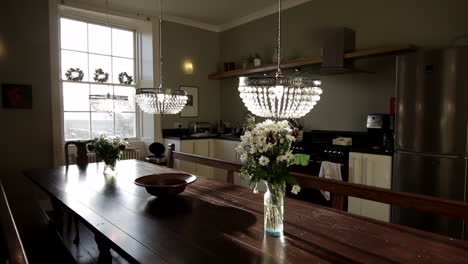 large kitchen banquet table with crystal pendant lights, a range cooker and a large window letting in sunlight