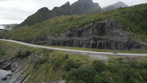 vista aérea que muestra un vehículo negro que se mueve a lo largo de un camino que serpentea a lo largo de las montañas y el océano en lofoten, noruega