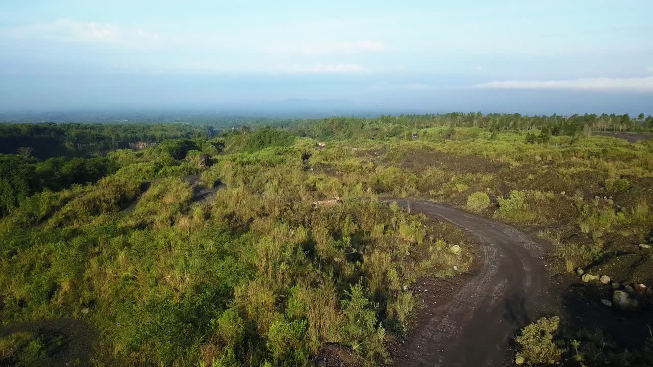 AERIAL flyover road on volcano with driving industrial trucks to sand mine in sunlight