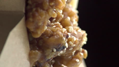 dutch angle vertical view of many sesame seeds sprinkled, garnished and dropped on, above and top of cooked mentai chicken chunks, black background, detail extreme close up static