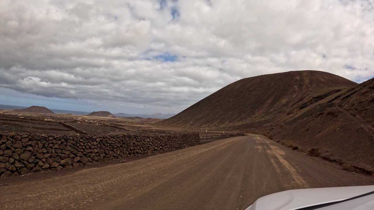 POV Perspective Driving a Vehicle Along Rugged Dirt Tracks in the Shadow of Massive Volcanic Mountains in Fuerteventura Spain for Adventure Video