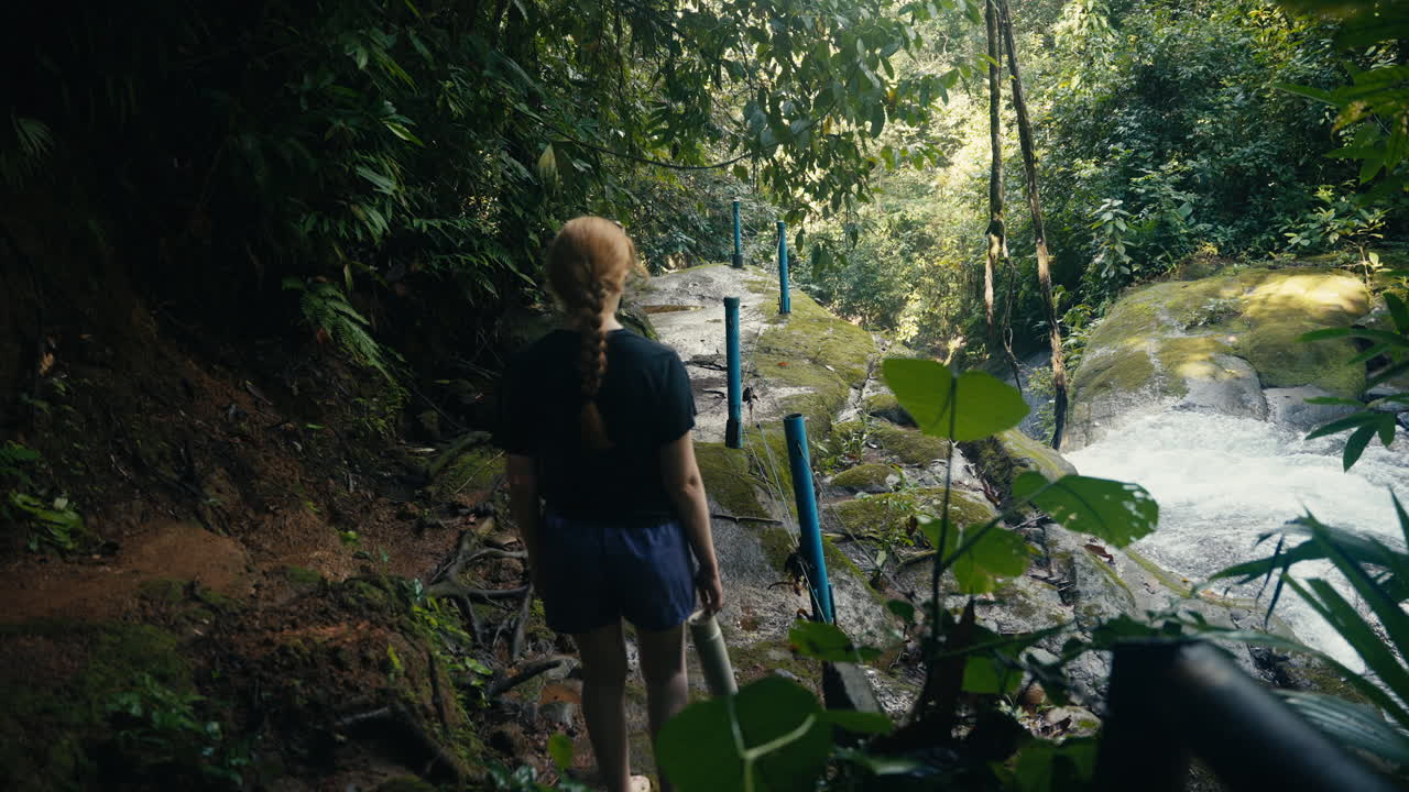 Woman walking along a jungle path near a waterfall