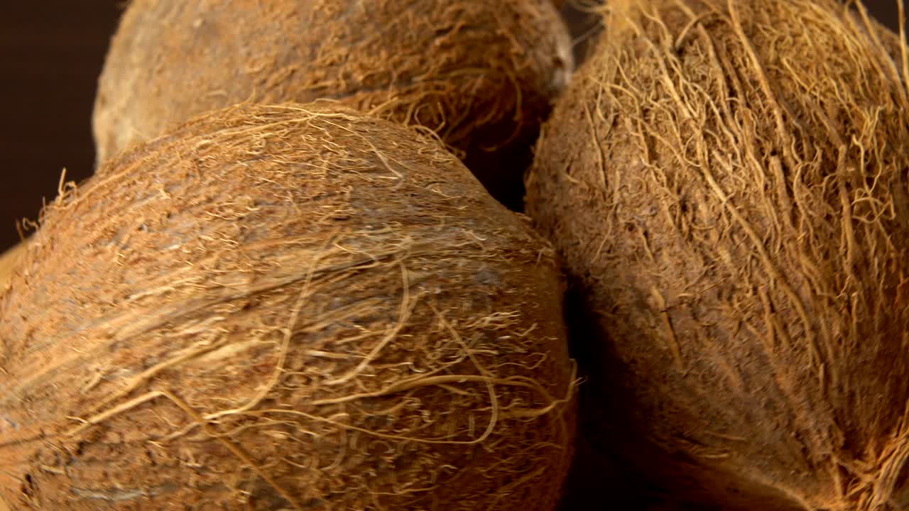 tres cocos tropicales maduros marrones girando sobre un fondo negro. frutas y alimentos tropicales. bucle