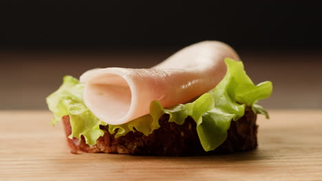 hand placing ham slice on a sandwich with lettuce