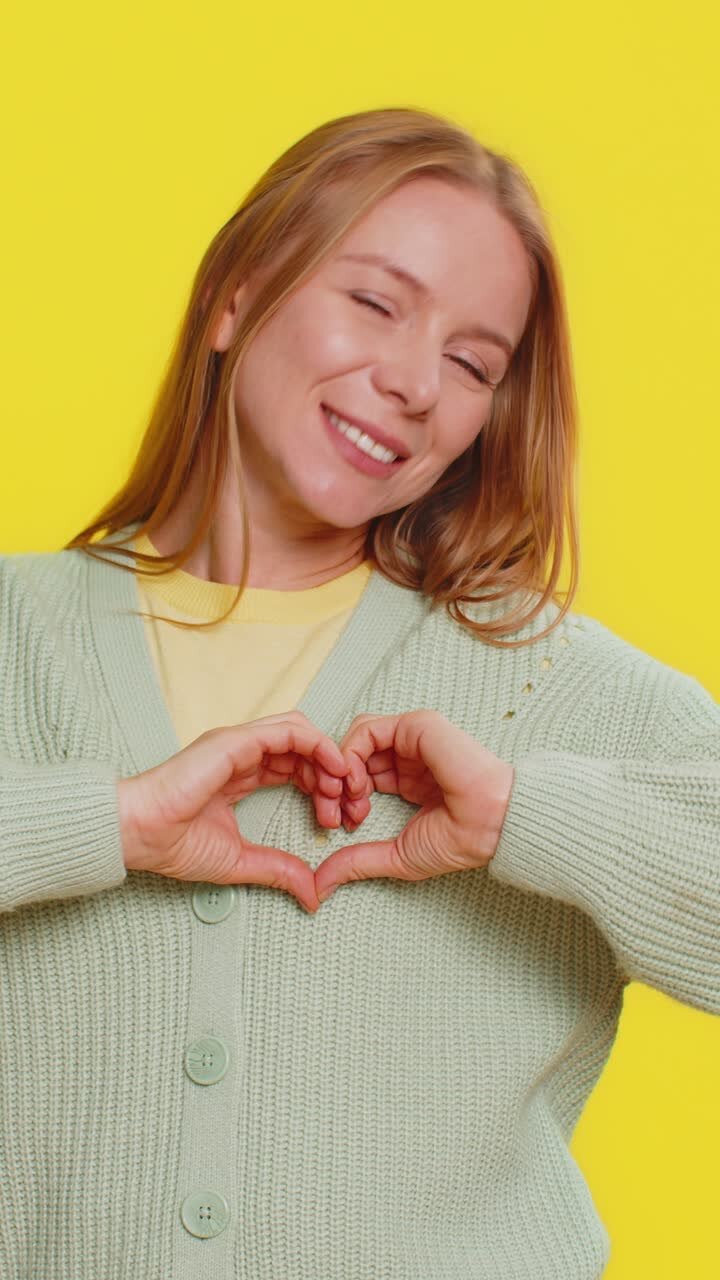 Una giovane donna sorridente fa un gesto con il cuore, dimostra il segno dell'amore, esprime buoni sentimenti e simpatia.